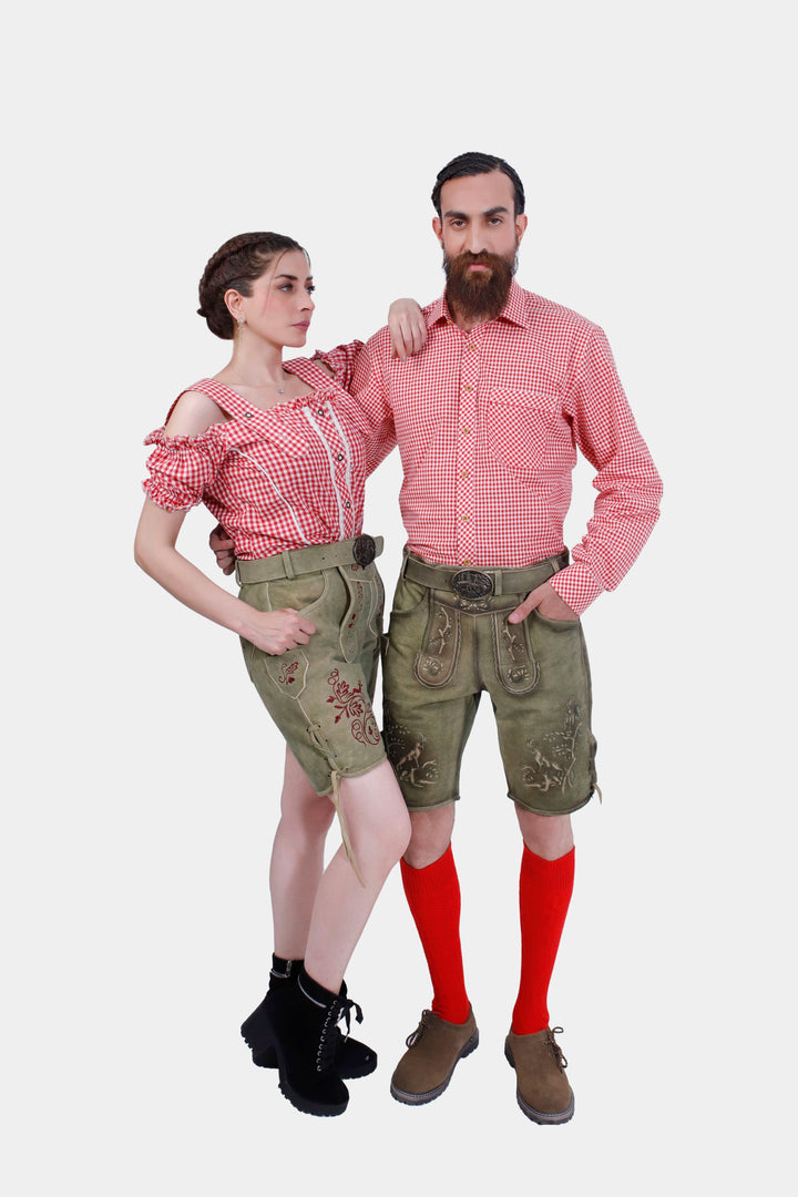 A couple wearing traditional German attire. The woman is dressed in a red and white checkered off-shoulder top with olive embroidered shorts. The man is in a matching red and white checkered shirt, olive embroidered shorts, red knee-high socks, and brown shoes. 