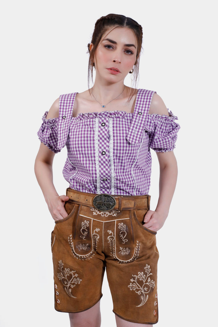 Close-up of the front of Angelina Lederhosen, showing the embroidery detail on the bib and front pockets, paired with a purple checkered blouse.