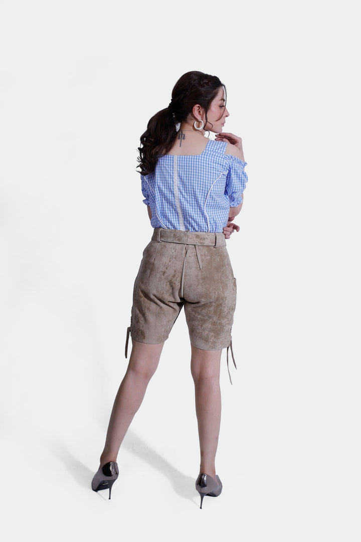 Rear view of a woman wearing light brown suede lederhosen and a blue and white checkered off-shoulder top, highlighting the fit and design from the back.