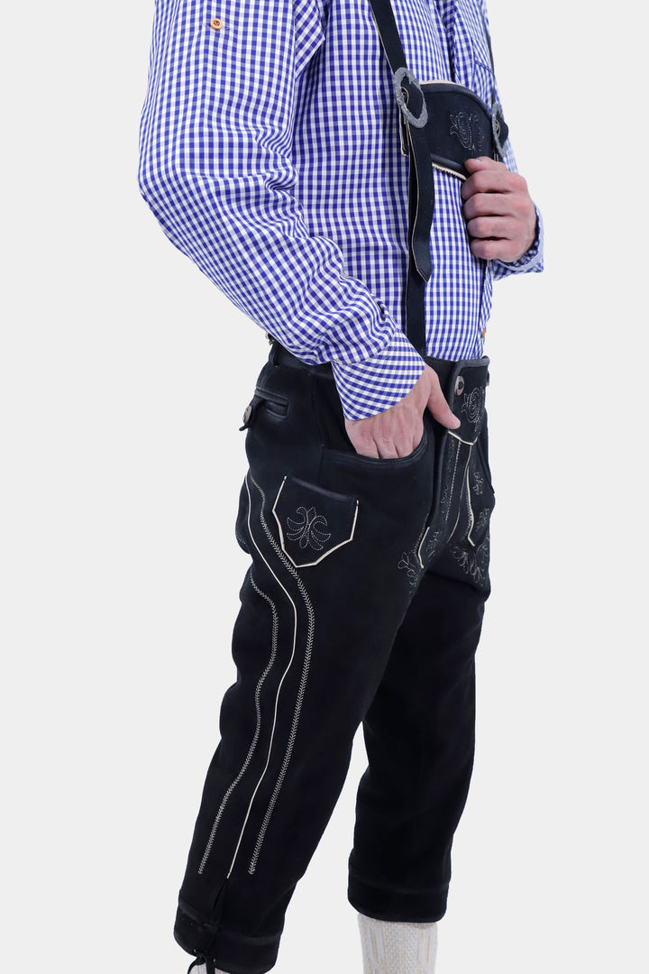 A detailed side view of the Brandburg Bundhosen Outfit, worn by a man. The focus is on the side pocket with an embroidered flap, the side seam embroidery. The man hands are in the pocket, showcasing the practical design of the pants. He is also wearing black shoes with socks.