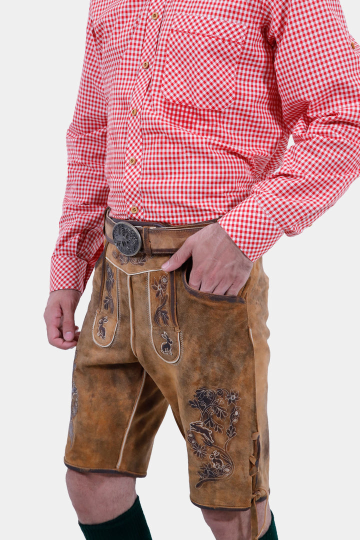 Angled close-up view of a man wearing Chiemsee Lederhosen and a pink checkered shirt, showing the belt and intricate embroidery on the leather shorts.