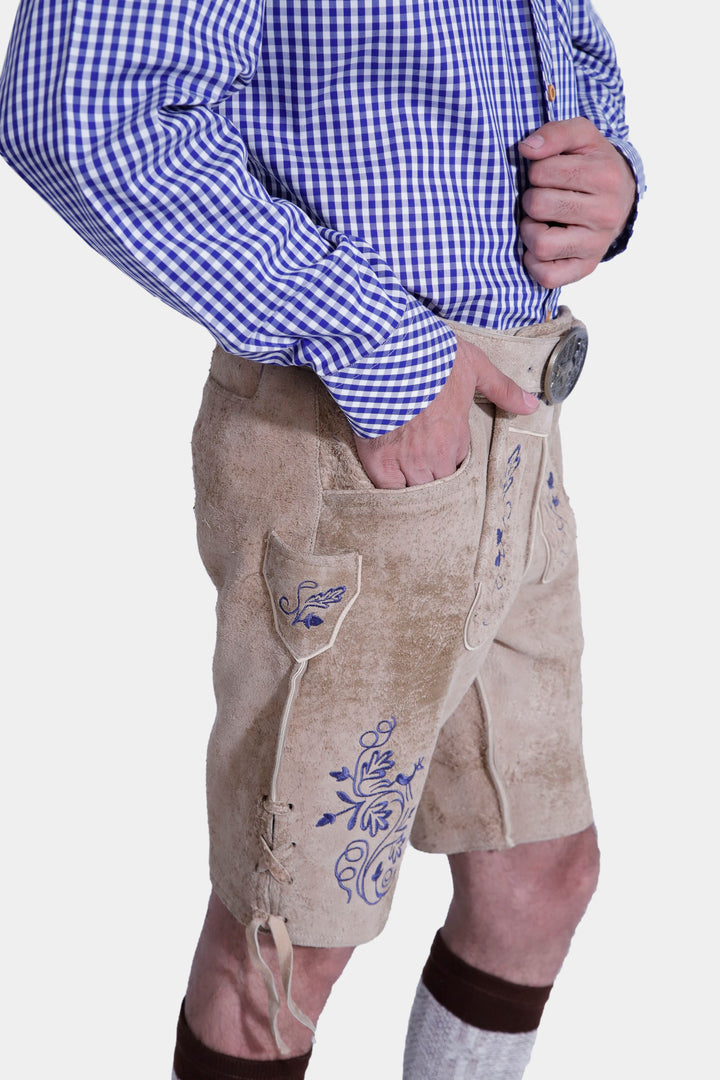 Side view of a man in beige-colored Cincinnati Lederhosen with a blue checkered shirt, showcasing the embroidered details and side laces of the traditional leather shorts. He is also wearing beige-colored shoes.