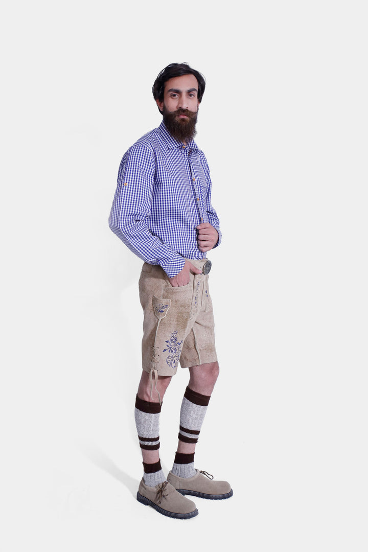 Three-quarter view of a man in beige-colored Cincinnati Lederhosen, showcasing the fit and traditional Bavarian style with embroidered details. The man is wearing a blue checkered shirt and beige-colored shoes.