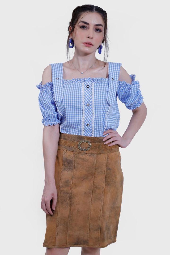 A woman is wearing a Clara Lederhosen skirt with a brown leather look, paired with a blue and white checkered off-shoulder blouse and nude high heels, standing against a plain white background.