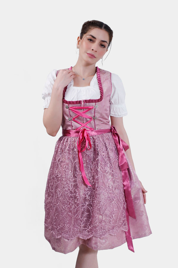 Woman posing thoughtfully in the Dirndl Christiane, featuring a pink lace bodice with intricate detailing and a flowing lace skirt. midi dirndl rosa , pinke dirndl