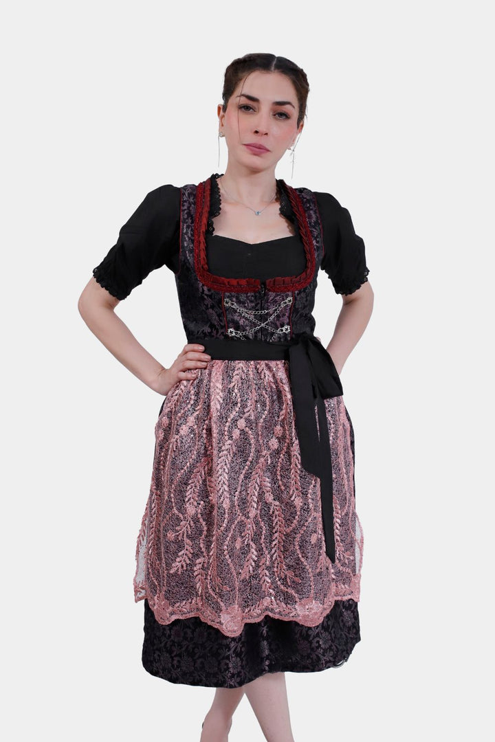 A woman in Dirndl Franka with a detailed black silk bodice, standing with hands on hips against a white background. dirndl schwarz