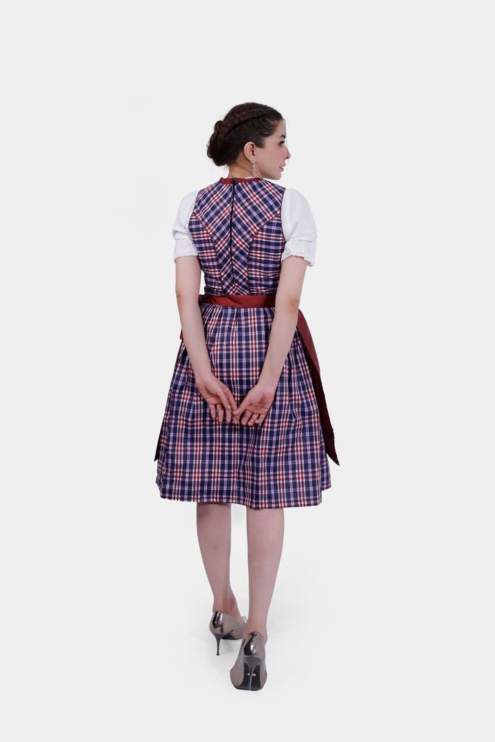 Back view of Dirndl Zsa Inci, displaying the intricate tie of the crimson apron against a plaid skirt.