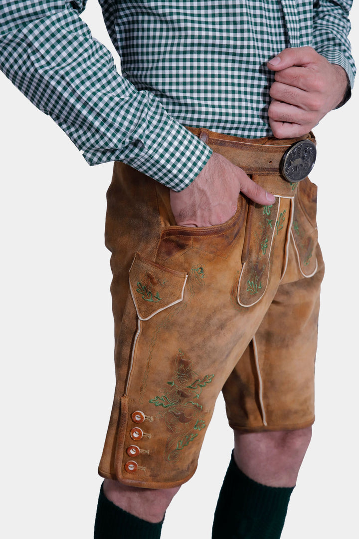 Angled view of a man in the Durant Lederhosen Outfit, highlighting the front pocket and button details on the brown leather Lederhosen with green embroidery.