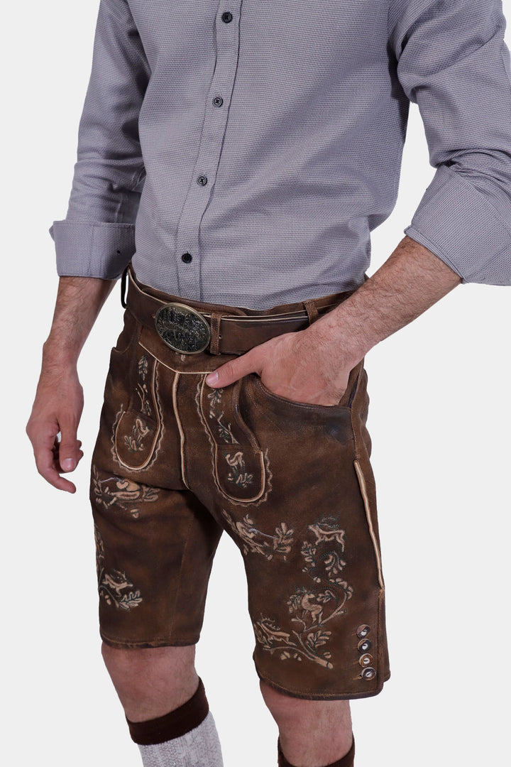 Man standing with one hand in pocket, wearing Ein Prosit Lederhosen, displaying the front embroidery and traditional design of the leather shorts.