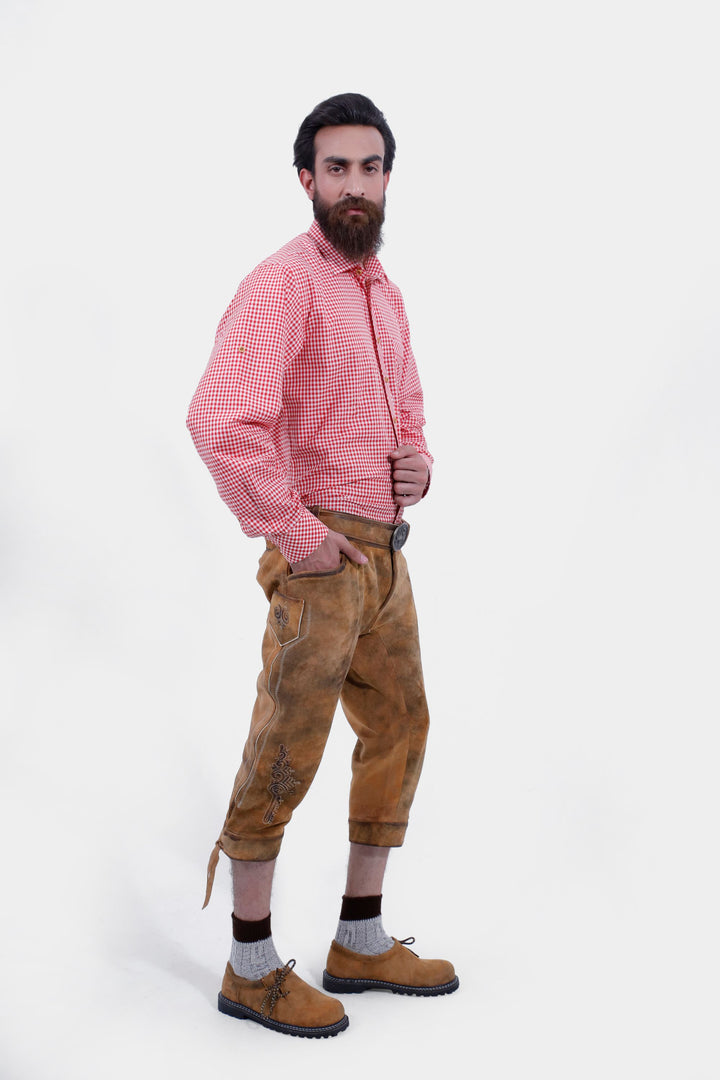 A bearded man wearing a white patterned shirt and Eltz Bundhosen, posing with his hand in his pocket. The lederhosen features detailed embroidery on legs, paired with traditional socks and brown shoes.