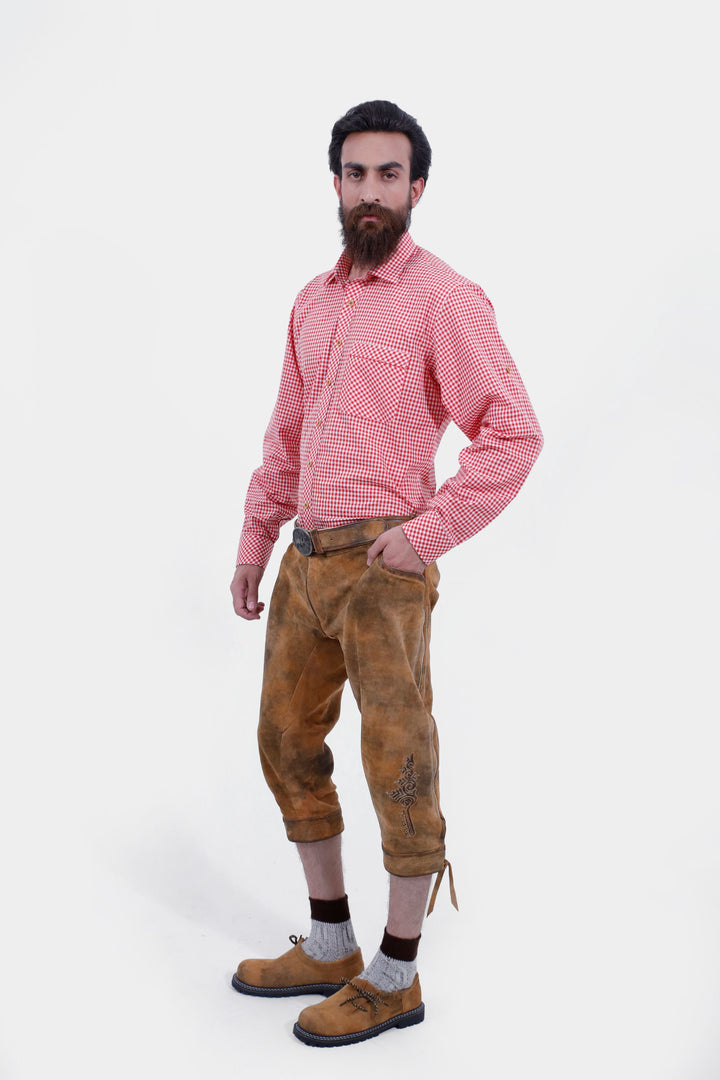 A bearded man wearing a white patterned shirt and Eltz Bundhosen, posing with his hand in his pocket. The lederhosen features detailed embroidery on legs, paired with traditional socks and brown shoes.