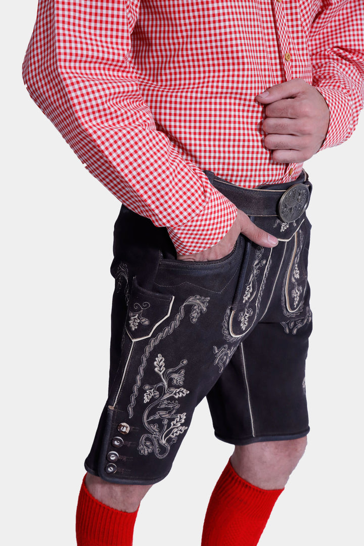 Close-up detail of the Everglades Lederhosen Outfit's white embroidered pocket on the black leather lederhosen, along with the red and white checkered shirt sleeve and hand resting in the pocket.