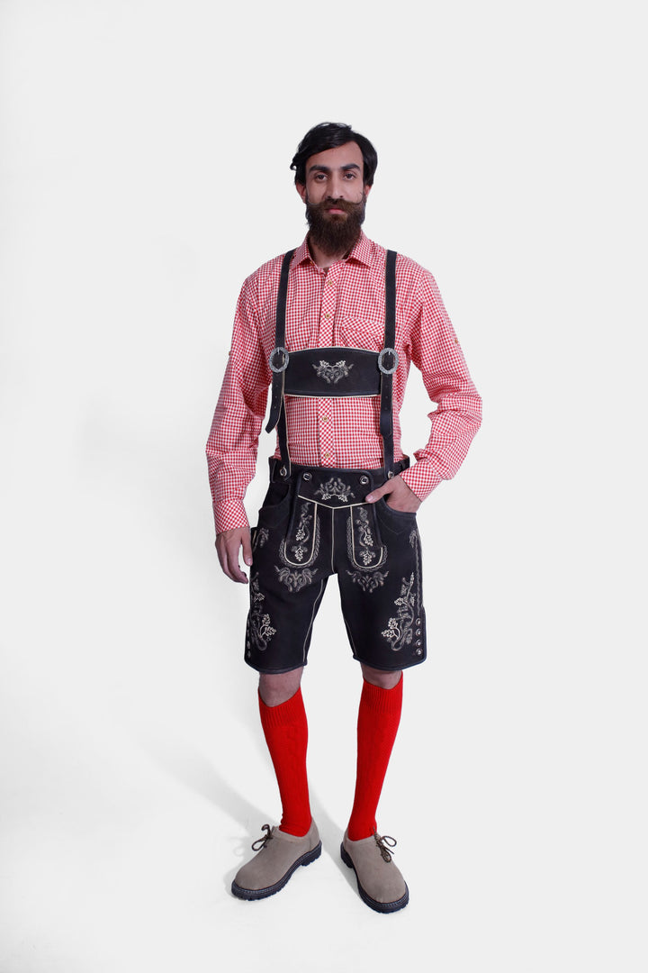 Full-body image of a man in an Everglades Lederhosen Outfit, featuring the red and white checkered shirt, black leather lederhosen with suspenders, white embroidery, red knee-high socks, and tan shoes.