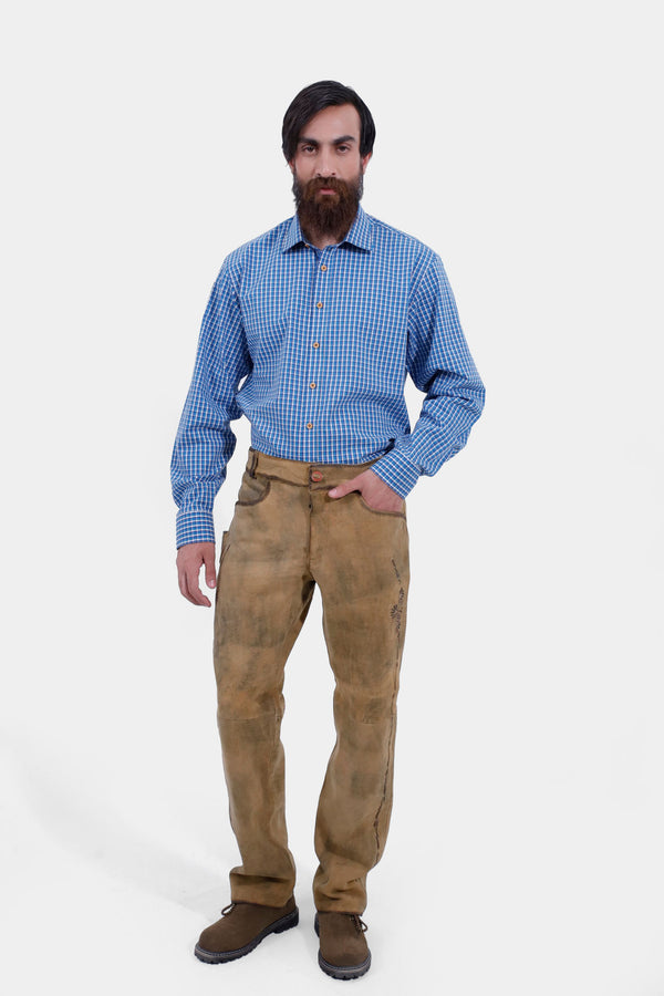 A man with a beard wearing a blue checkered shirt and tan Goretzka lederhosen. He is standing with a neutral expression, hands by his side, showcasing the full outfit. lederhose herren lang