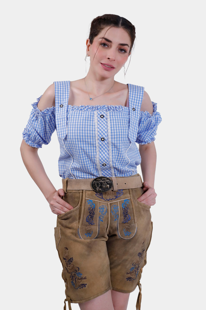 Woman wearing Helene Fischer Lederhosen, posing with hands in pockets, featuring detailed embroidery and a blue checkered blouse.