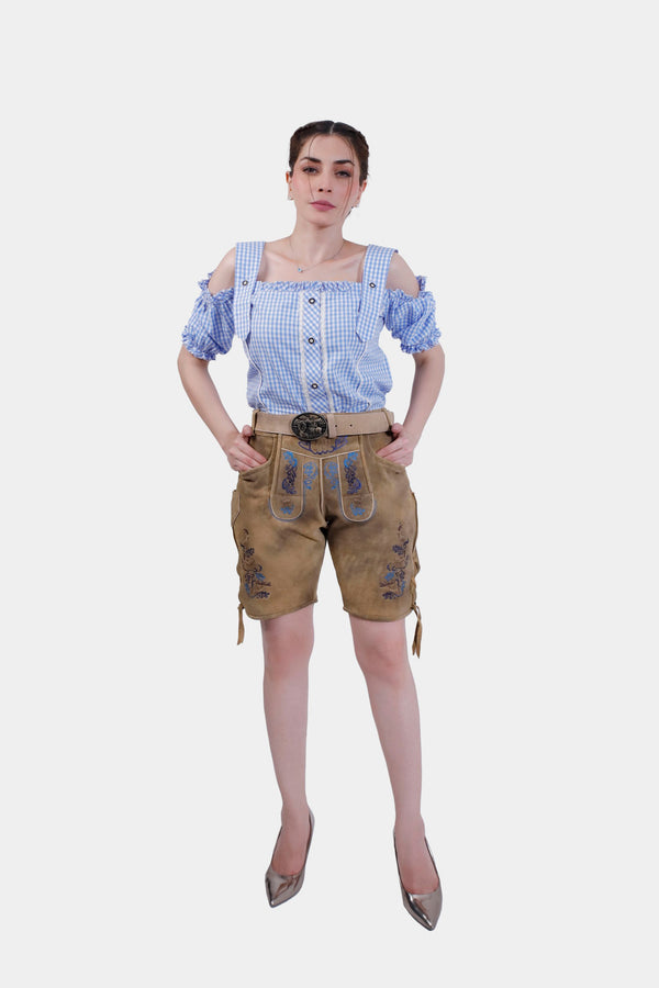 Full body front view of woman wearing Halen Fischer Lederhosen, posing confidently with hands in pockets and wearing a blue checkered blouse. Damen Lederhose Kurz