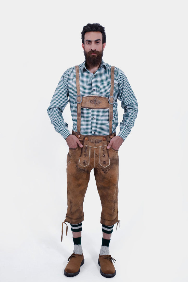 Front view of a man wearing a green checkered shirt and Hesse Bundhosen with suspenders. The brown leather pants have intricate floral embroidery on the front, side pockets, and are paired with traditional Bavarian shoes and green-striped socks.