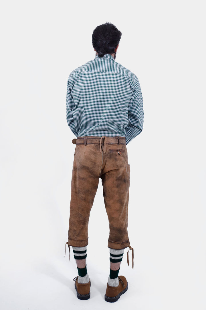 Back view of a man in a green checkered shirt and Hesse Bundhosen. The brown leather pants feature a waistband, back pockets, and detailed embroidery. He is wearing traditional Bavarian shoes and green-striped socks.