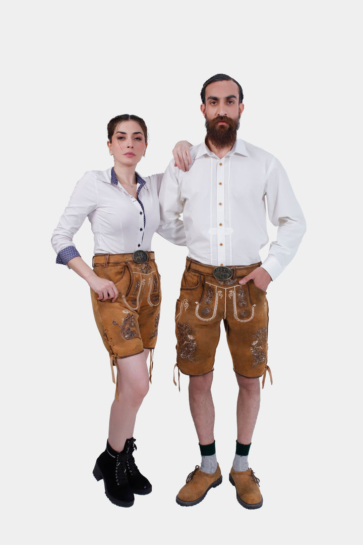 A couple wearing traditional German outfits. The woman is dressed in a white blouse with blue accents and tan leather shorts with floral embroidery. The man is wearing a white button-down shirt with tan leather shorts featuring floral embroidery, green socks, and brown leather shoes. trachtenpaar outfit , partner outfit​