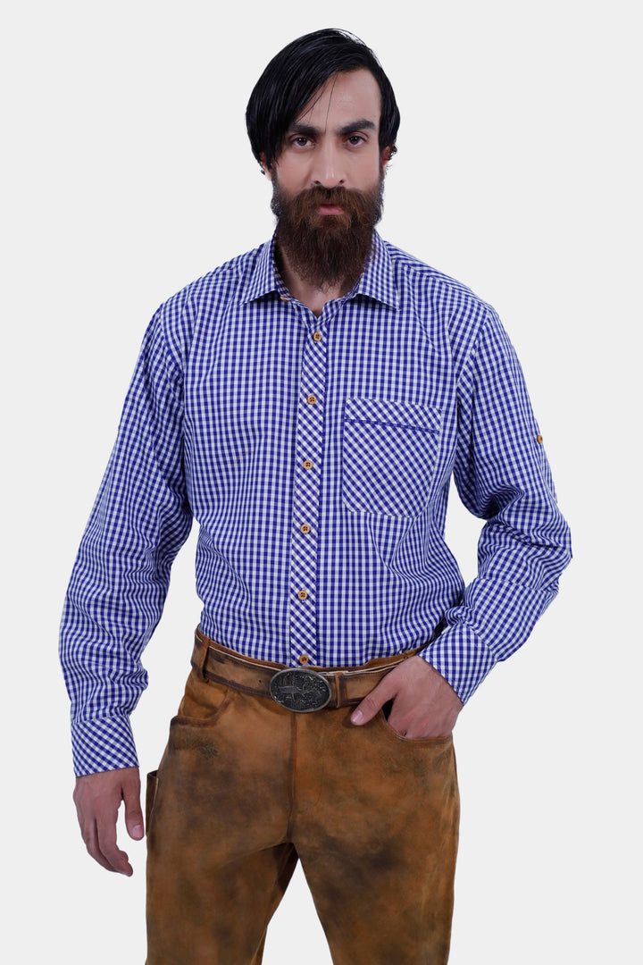 A close-up image of a bearded man with black hair wearing a blue and white checkered shirt and Humboldt Long Lederhosen, with his hand in the pocket of the pants