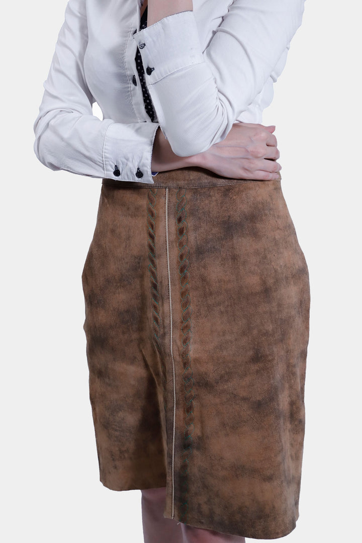 Close-up front view of a woman wearing the IRINA Lederhosen Skirt in brown leather paired with a white button-up shirt, focusing on the skirt's embroidery and texture.