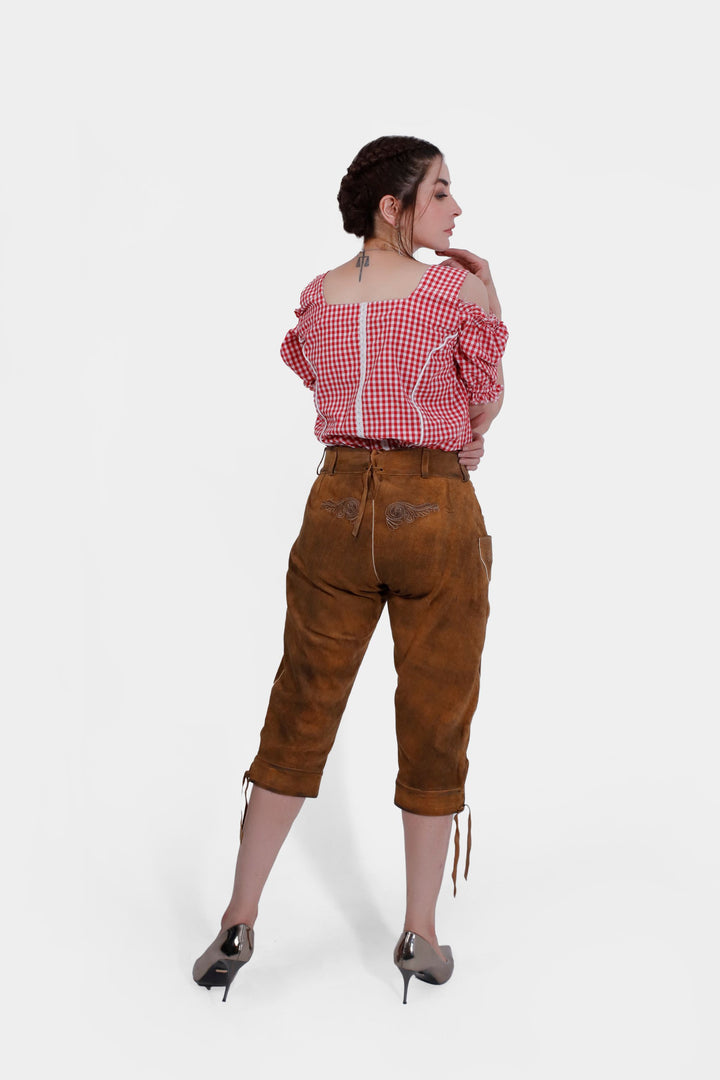 The same woman is seen from the back. She is wearing a red and white checkered, off-shoulder blouse with ruffled sleeves and the "Kirsten Dunst Lederhosen" brown leather pants. Her hair is braided, and she is looking over her shoulder.