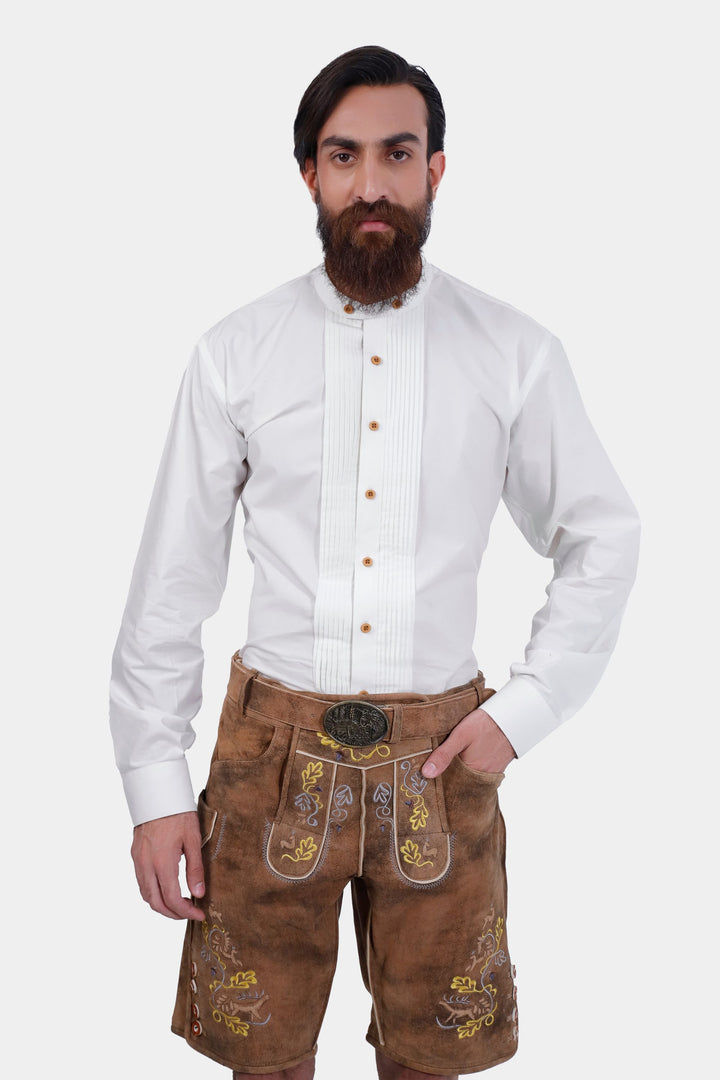 A man with a beard is wearing traditional Leavenworth lederhosen and a white shirt with wooden buttons. The lederhosen are decorated with yellow and green embroidery and a decorative belt buckle.