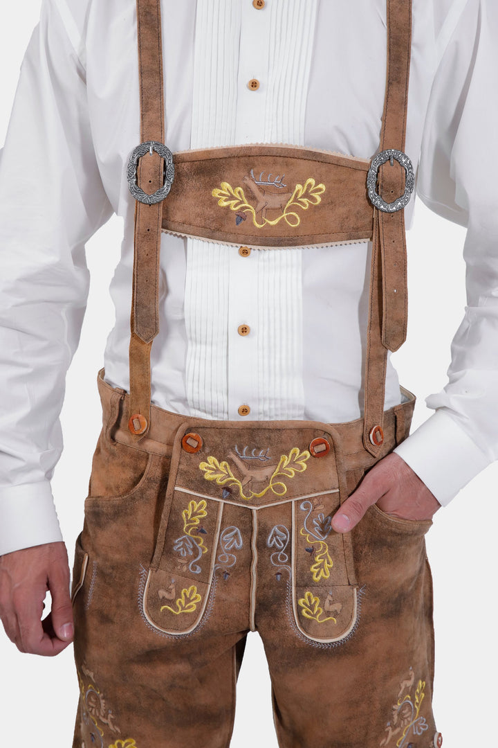 Close-up of a man wearing Leavenworth lederhosen with suspenders. The suspenders are adorned with a silver buckle, and the lederhosen feature intricate yellow and green embroidery.