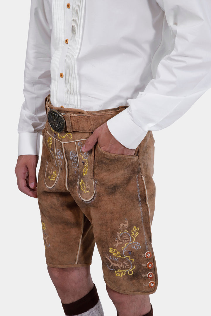 Side view of a man wearing Leavenworth lederhosen. The lederhosen are light brown with yellow and green embroidery, and the man has his hand in his pocket.