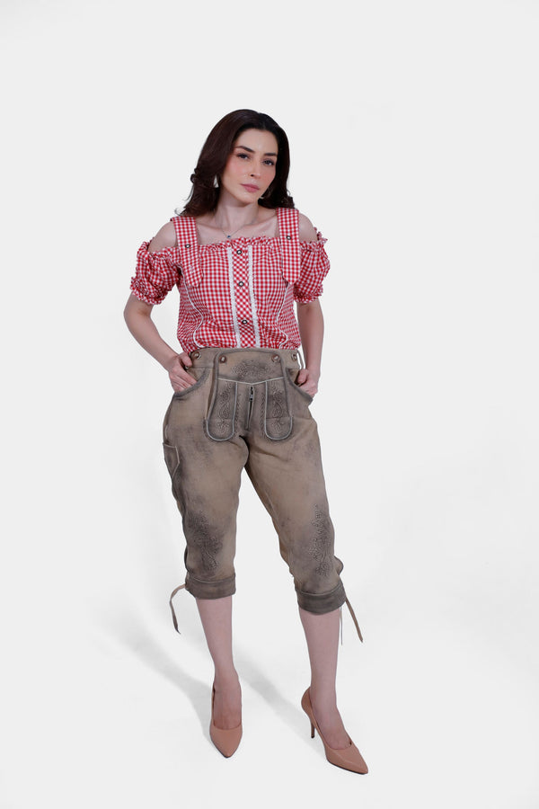 Full-body front view of the woman in a red checkered blouse and brown lederhosen, standing with her hands in her pockets. Knielang Lederhose Damen, damen lederhose knielang