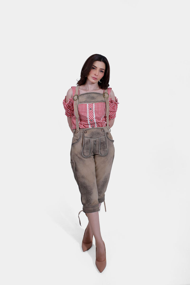 Another full-body view of the woman in a red checkered blouse and brown lederhosen, posing with one hand on her hip.