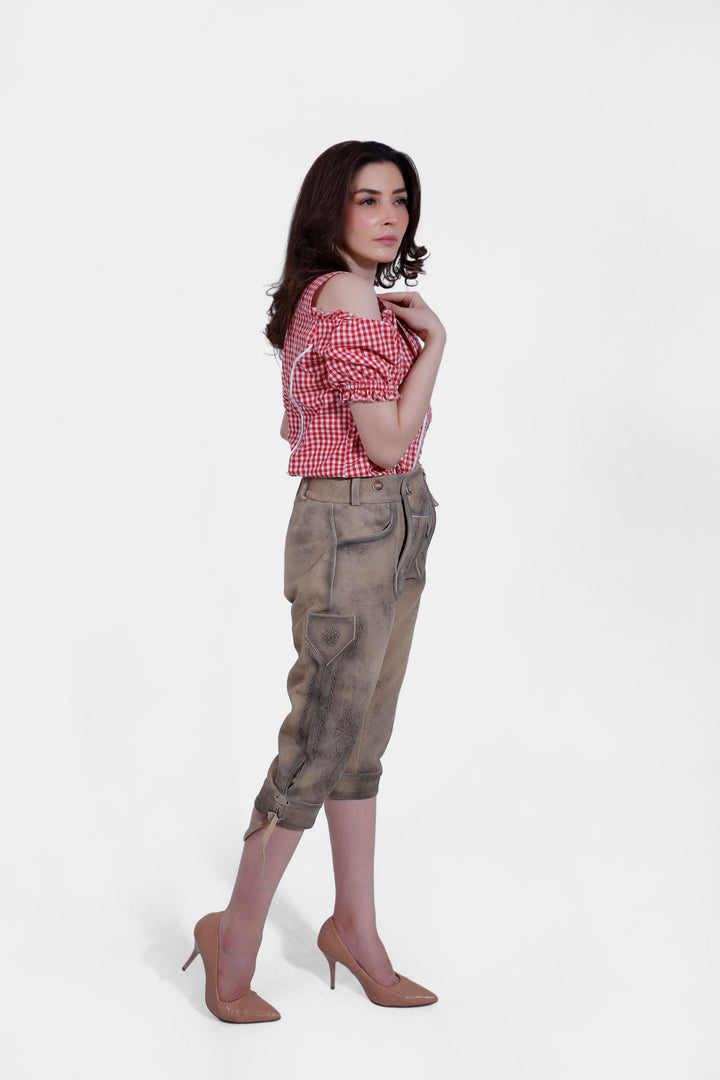 Rear view of the woman in a red checkered blouse and brown lederhosen, highlighting the back design of the pants and blouse.