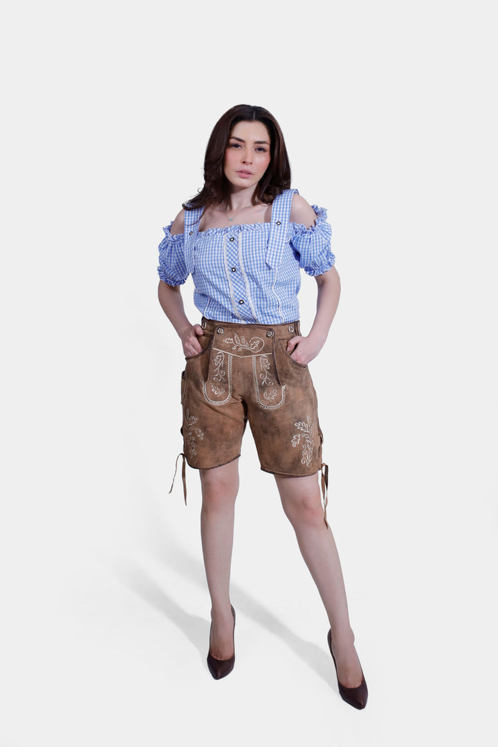 Full body front view of woman wearing Lorelei Lederhosen, posing confidently with hands in pockets and wearing a blue checkered blouse. lederhose oktoberfest damen günstig