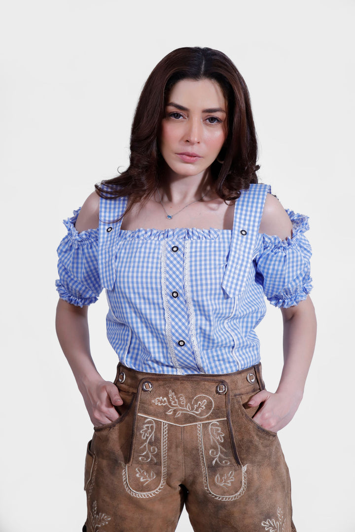 Woman wearing Lorelei Lederhosen, posing with hands in pockets, featuring detailed embroidery and a blue checkered blouse.