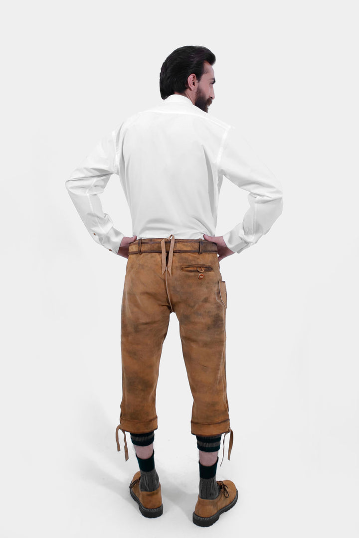 Rear view of a man wearing Lothar Bundhosen Outfit. He is dressed in a white traditional shirt and brown bundhosen with detailed embroidery, showcasing the back design.