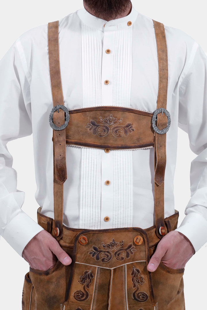 Close-up of a man wearing Lothar Bundhosen Outfit with suspenders. The focus is on the white traditional shirt and the detailed brown bundhosen with ornate embroidery and suspenders.