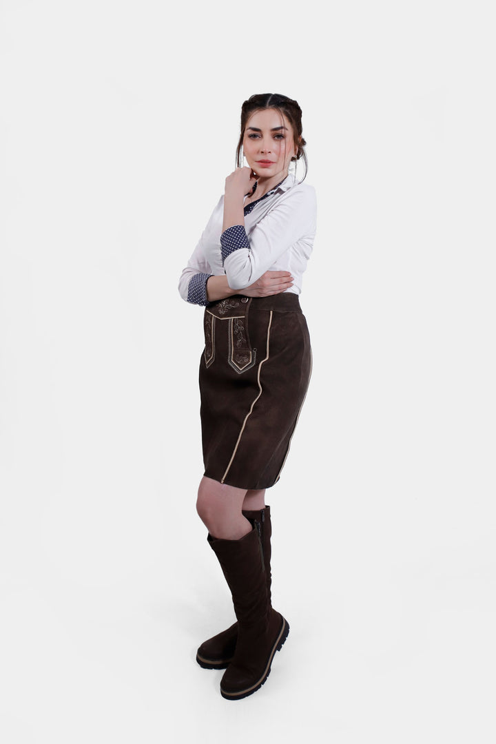 Close-up view of the Louise Lederhosen Skirt in dark brown leather worn by a woman, showcasing the intricate white embroidery detail and buttons on the front