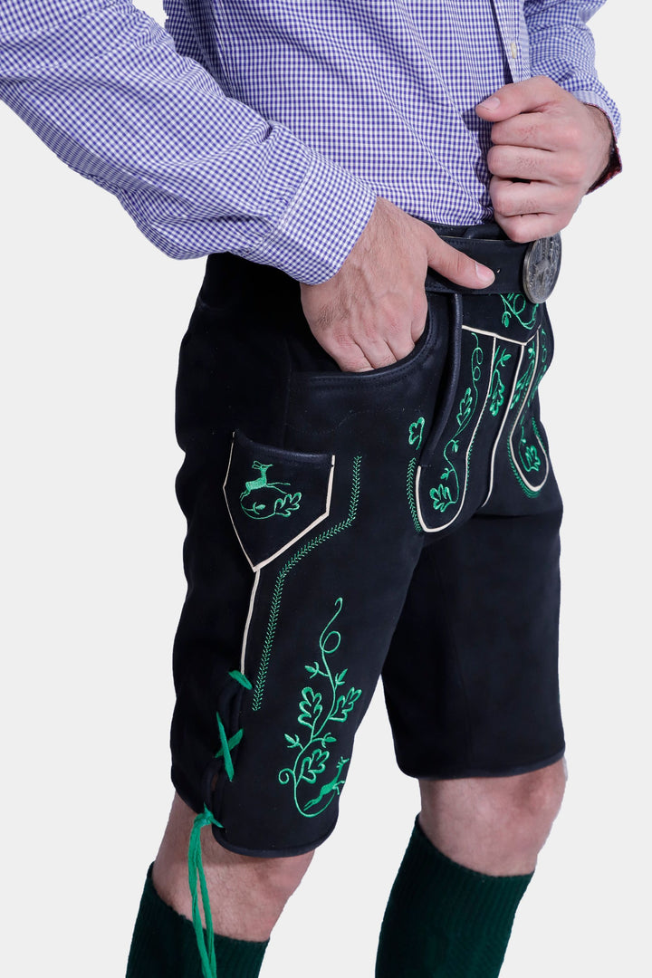 Side view of the Melk Abbey Lederhosen Outfit, focusing on the detailed green embroidery on the black leather lederhosen, paired with a purple checkered shirt and hand in the pocket.