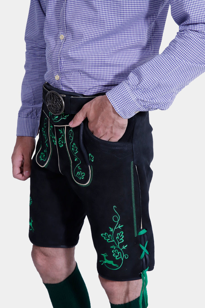 Close-up detail of the Melk Abbey Lederhosen Outfit's green embroidered pocket on the black leather lederhosen, along with the purple checkered shirt sleeve and hand resting in the pocket.