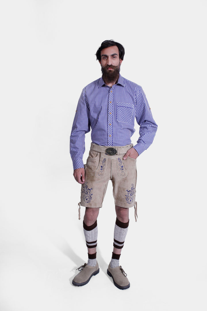 Full-body view of a man in a Mookie Lederhosen Outfit, showcasing the blue and white checkered shirt, tan leather lederhosen with blue embroidery and suspenders, knee-high socks, and tan shoes. trachten outfit herren​ , trachten lederhose herren