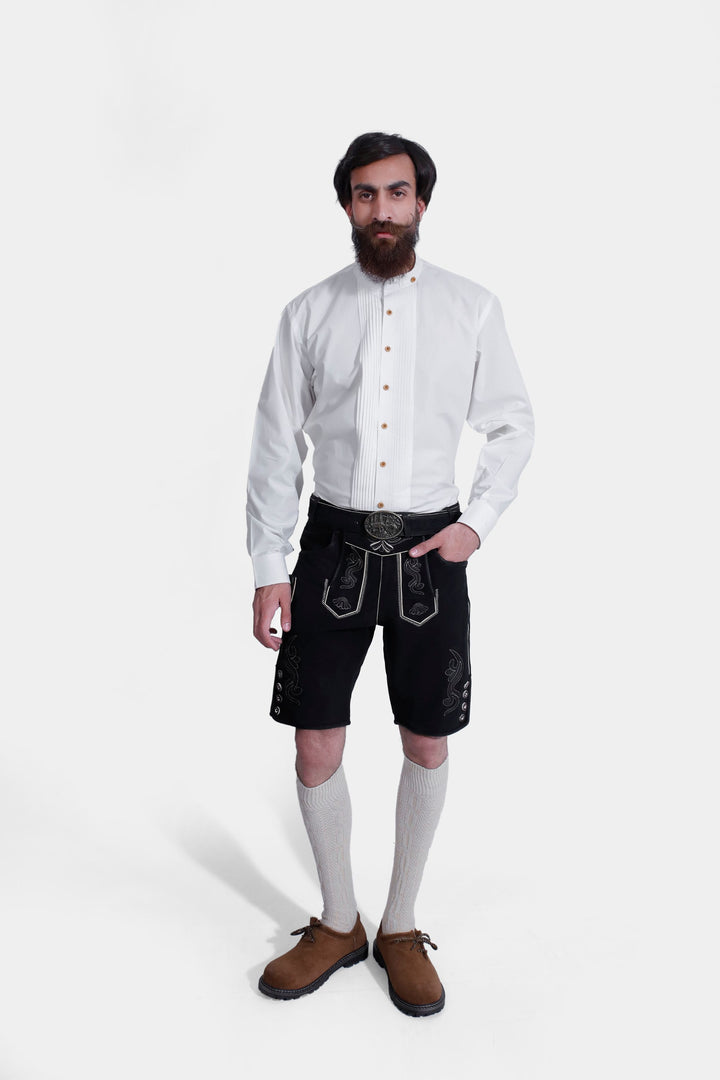 Man in traditional German attire, wearing Oktoberfest Appleton Lederhosen, paired with a crisp white shirt and brown shoes, standing against a white background. He is accessorized with adjustable suspenders and showcases detailed Alpine embroidery on the black leather shorts. herren lederhosen schwarz, kurze schwarze lederhose​