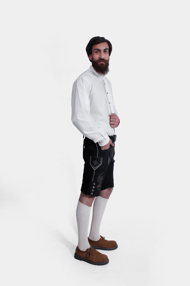 Man wearing traditional black lederhosen with elegant Alpine patterns, paired with a white shirt and brown leather shoes.