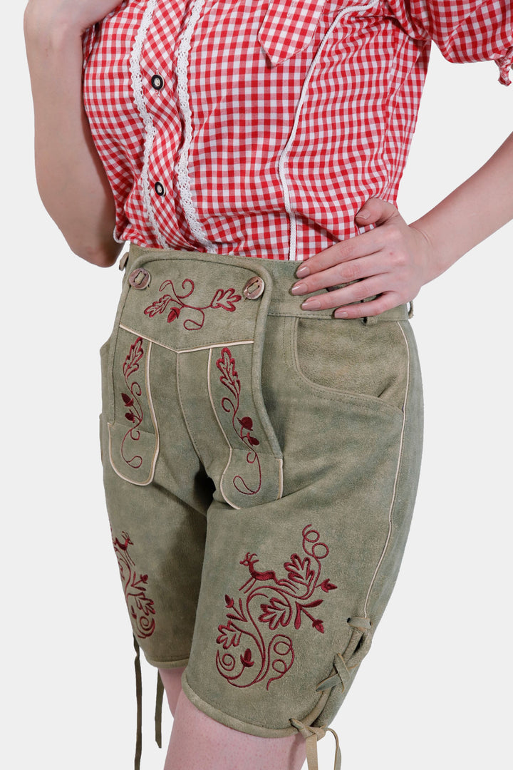 Side view of a woman in Olivia Charm Lederhosen, highlighting the knee-length fit, two front pockets, and intricate embroidery on the legs.