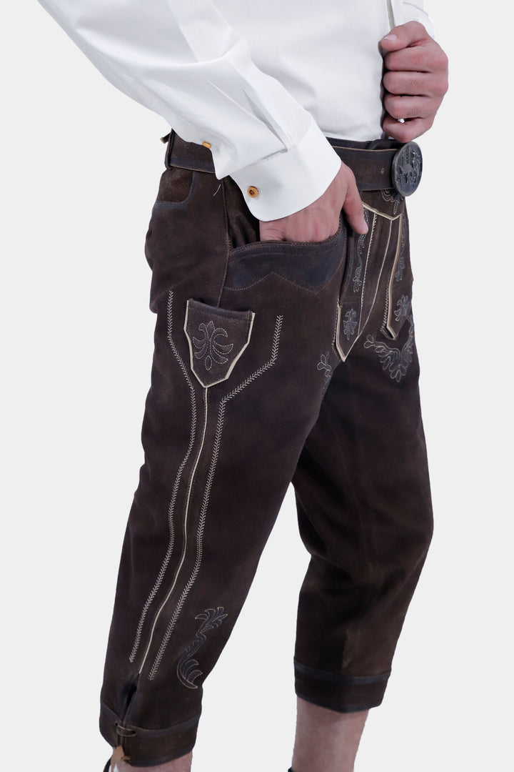 A close-up view of Philipp Lahm Bundhosen Outfit, focusing on the detailed embroidery and decorative belt buckle. The man is wearing a white button-down shirt, with his hands casually placed in the pockets of the Bundhosen.