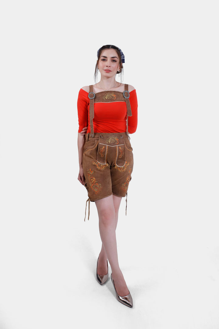 Woman posing in Queen Victoria Lederhosen, demonstrating the intricate embroidery and brown horn buttons on the bib, paired with a red top.