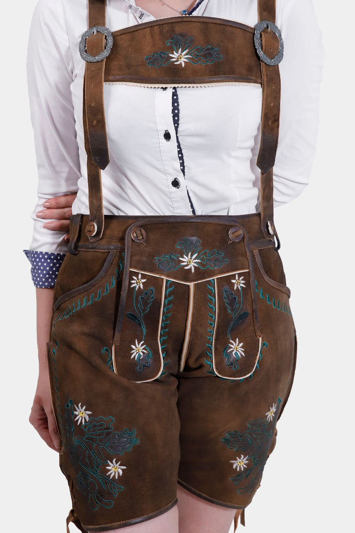 Woman wearing Romy Schneider lederhosen in Rustic Oak, showcasing the detailed natural color embroidery on the bib and legs, paired with a white button-up shirt.