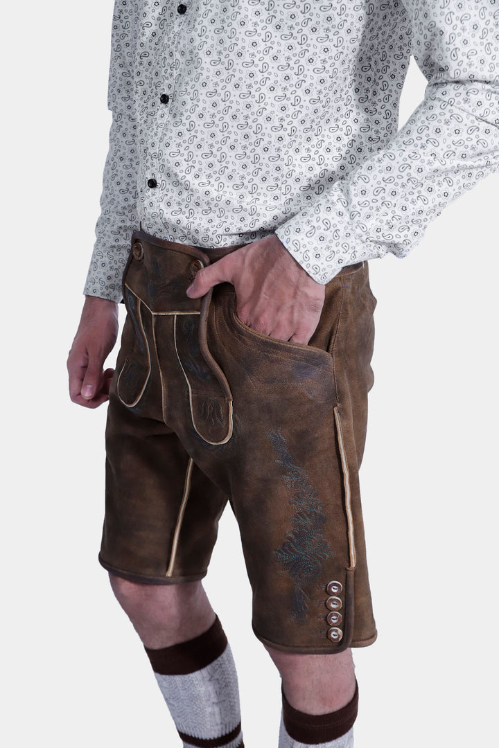 Side view of brown leather lederhosen featuring detailed embroidery and buttons, worn by a man against a white background.