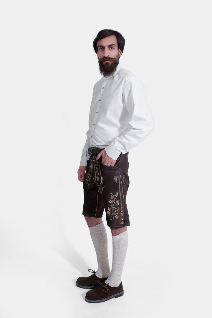 Side profile of a model in Spiegel Lederhosen, showing the detailed embroidery and side buttons on the leather shorts, paired with a white shirt and knee-high socks