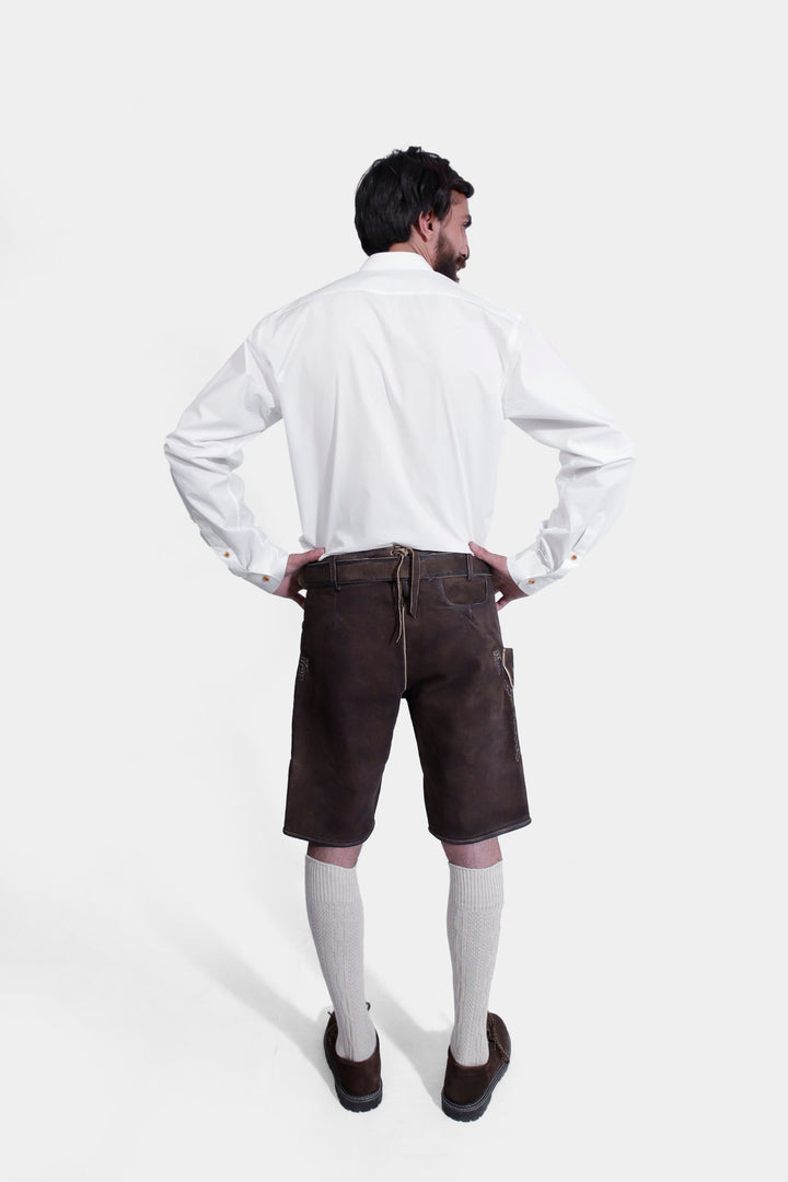 A man in a traditional white Bavarian shirt and brown Spieth Lederhosen outfit, viewed from the back, showing the detailed stitching and embroidery on the Lederhosen