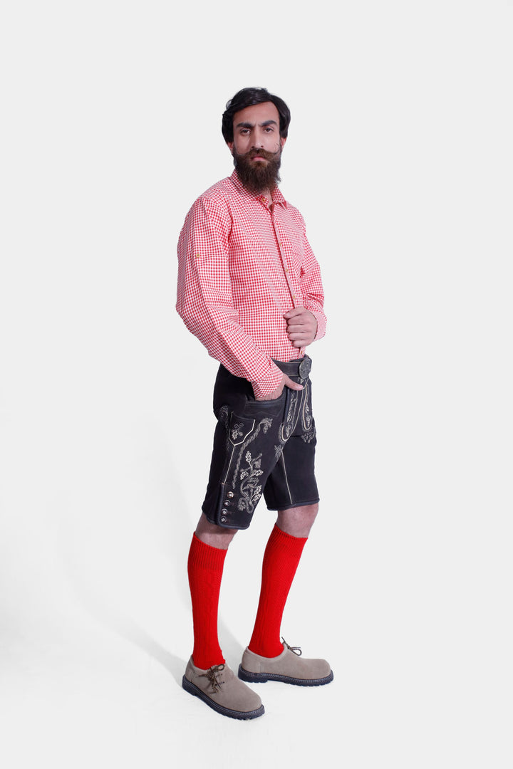 Three-quarter view of a man in Steuben Lederhosen, showcasing the fit and traditional Bavarian style with embroidered details. The man is wearing a red checkered shirt, red socks, and beige-colored shoes.